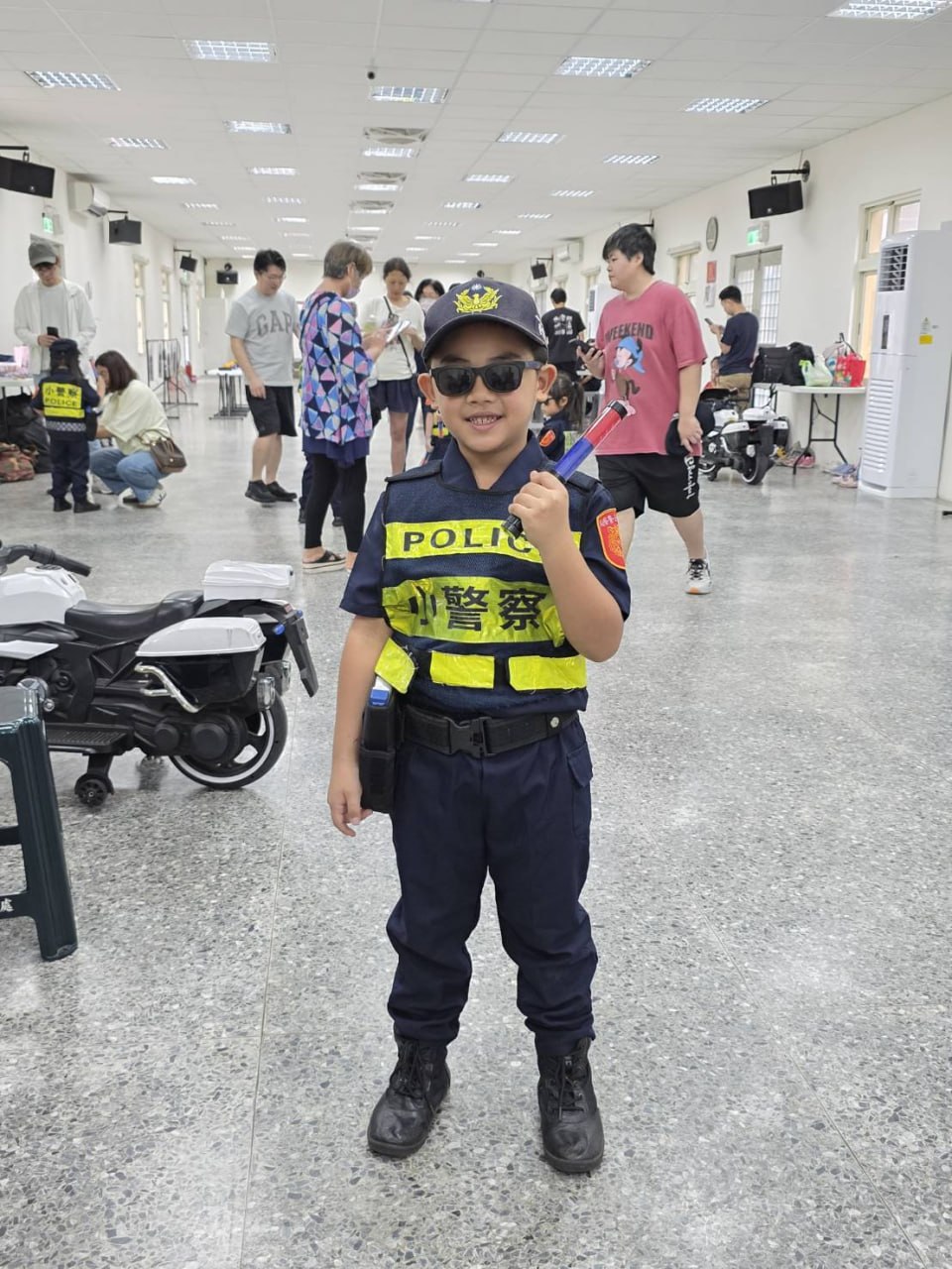 小小警察戴著墨鏡手持指揮棒站在警用機車旁