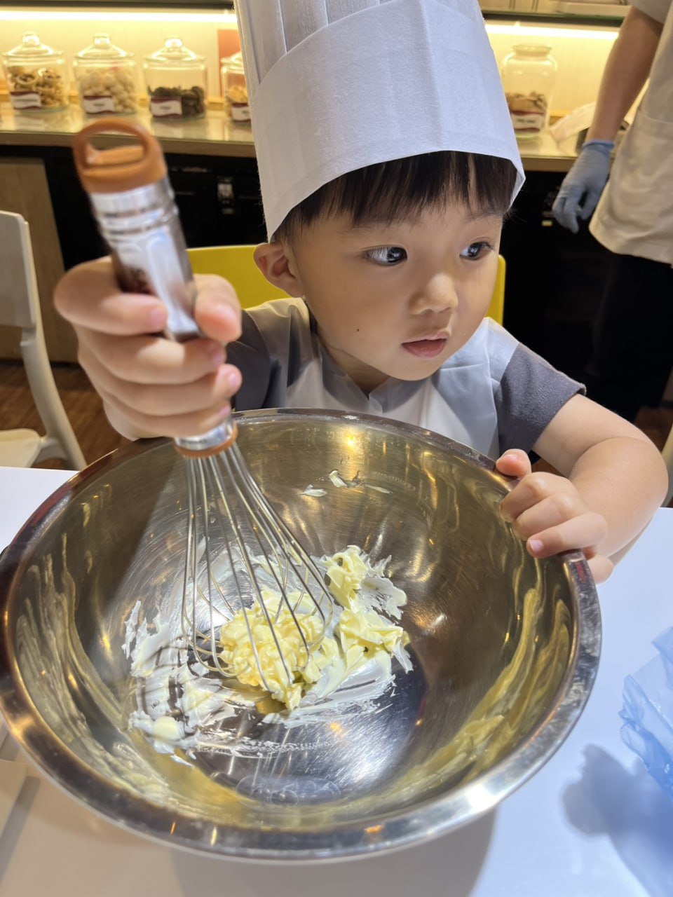 戴著廚師帽的孩子專注地攪拌鋼盆裡的麵糊
