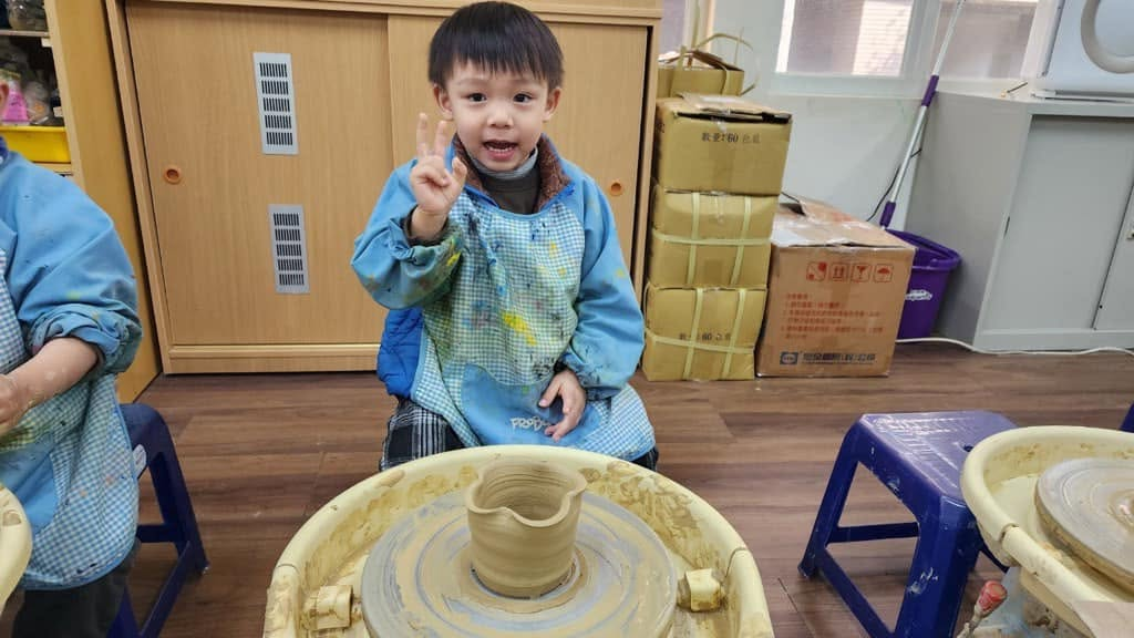 孩子完成陶土作品後開心比出勝利手勢