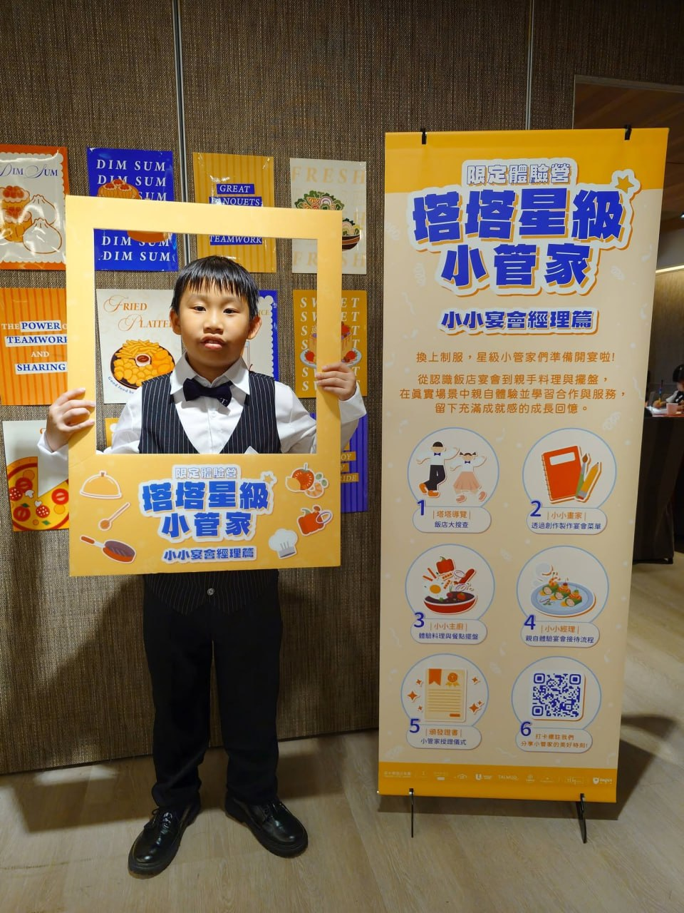 小小宴會經理拿著相框在活動海報旁留影