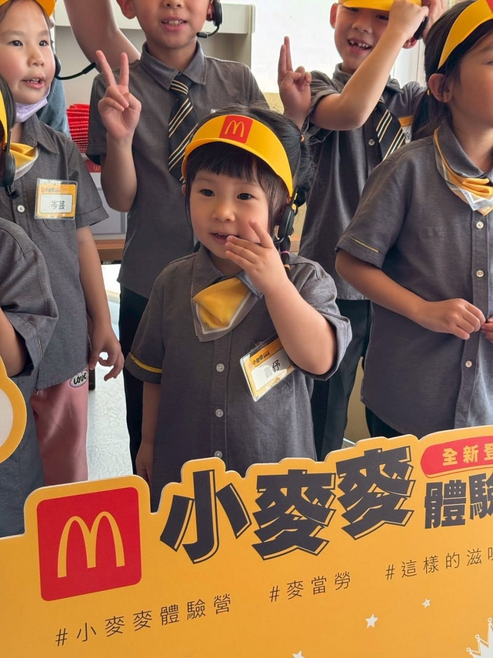 孩子們穿著小小店員制服在體驗營立牌前開心合照